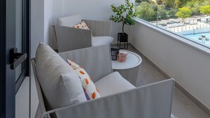 Een balkon met een bank en stoelen, een kleine tafel met een plant erop, en uitzicht op een zwembad en bergen.