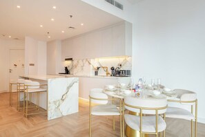 A modern kitchen with marble countertops, gold bar stools, and a dining table set for six.
