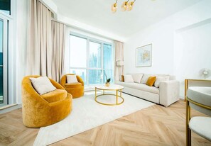 A modern living room with a sofa, two armchairs, a coffee table, and a large window with curtains.
