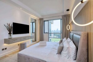 A modern bedroom with a large bed, a flat-screen TV mounted on the wall, and a city view through the window.