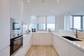 A modern kitchen with white cabinetry, a stainless steel oven, a microwave, and a large window providing a view of the city.
