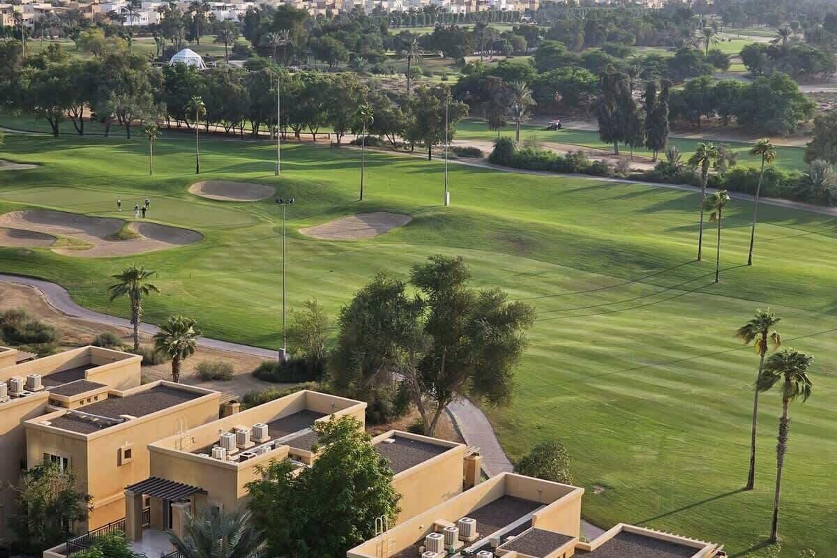 Un campo de golf con búnkeres de arena, palmeras y un edificio con unidades de aire acondicionado.