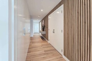 Un pasillo con piso de madera, una pared blanca con diseño de paneles verticales de madera y una puerta blanca con un pequeño ventanal.