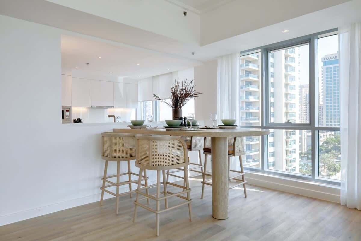 Una cocina moderna con una isla central, taburetes de bar y un ventanal que ofrece vistas a edificios altos.