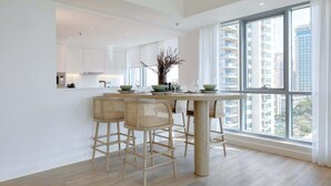 Een moderne keuken met een centraal kookeiland, barkrukken en een groot raam met uitzicht op hoge gebouwen.