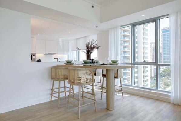 A modern kitchen with a central island, bar stools, and a large window offering a view of high-rise buildings.
