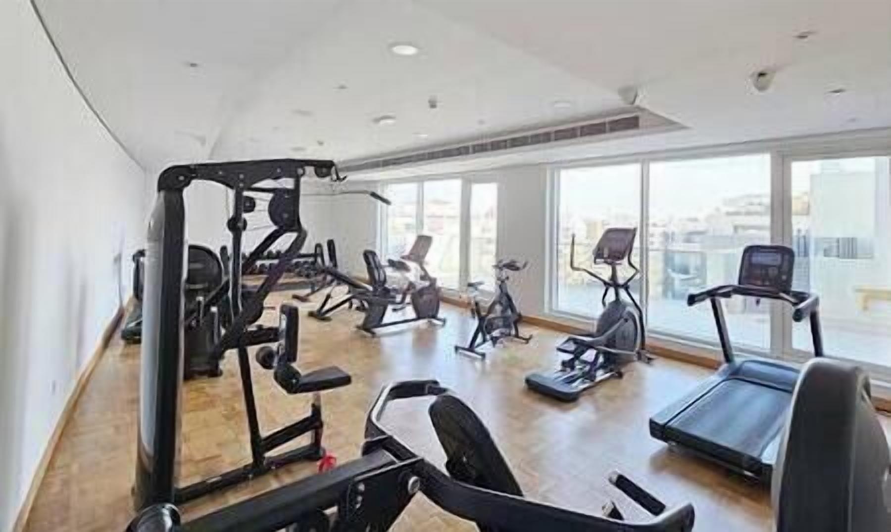 A gym with various exercise equipment, large windows, and a high ceiling.