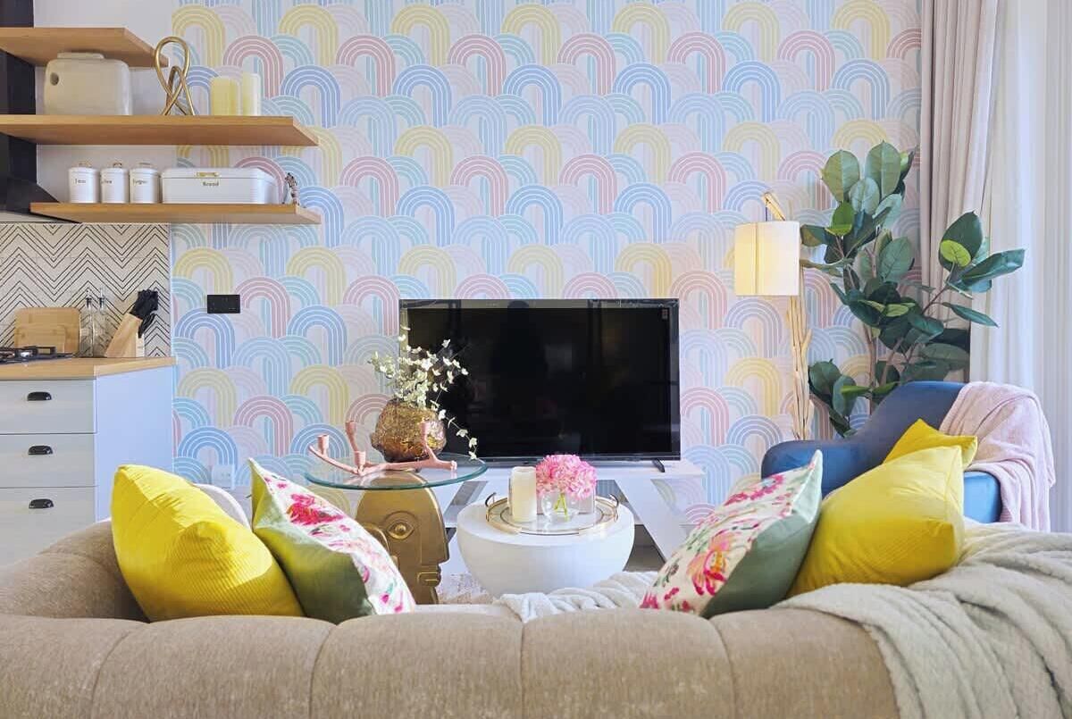 A living room with a sofa, a coffee table with a vase, a flat-screen TV, and a wall with a colorful pattern.