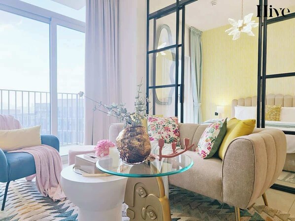 A modern living room with a glass coffee table, a sofa, and a bed with a striped wall in the background.