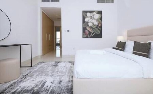 Ein modernes Schlafzimmer mit einem großen Bett, einem Nachttisch, einem an der Wand hängenden Kunstwerk und einem Flur, der in einen anderen Raum führt.