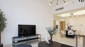 A modern living room with a flat-screen TV, a round coffee table, and a dining area with a chandelier.