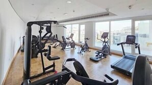 A gym with various exercise equipment, large windows, and a wooden floor.