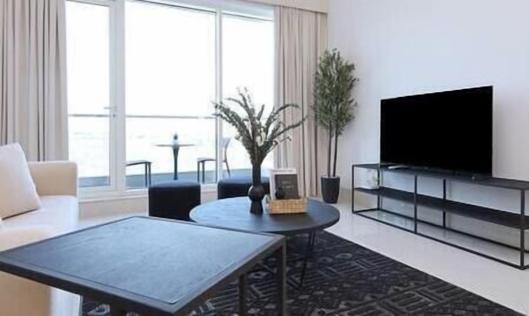A modern living room with a flat-screen TV, a sofa, a coffee table, and a potted plant.