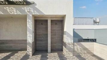 A building entrance with a double door, a concrete wall, and a shadow pattern on the ground.
