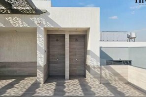 A building entrance with a double door, a concrete wall, and a shadow pattern on the ground.