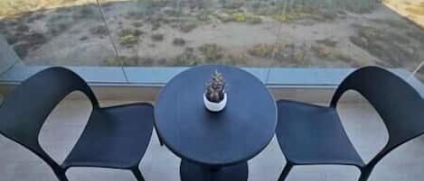 Un balcon avec deux chaises et une table, une plante en pot sur la table, et une vue sur un paysage désolé.