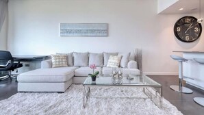 A modern living room with a sectional sofa, a glass coffee table, and a large wall clock. - Golf Course Views Apt W Pool & Fast Wifi (Dubai)