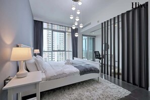 A modern bedroom with a large bed, bedside lamps, a fluffy rug, and a view of the city through large windows. - Golf Course Views Apt W Pool & Fast Wifi (Dubai)