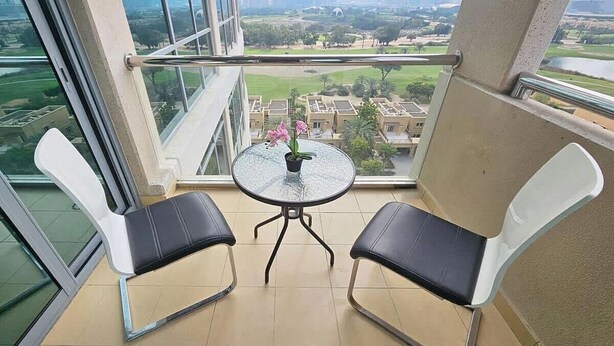 A balcony with two chairs and a small table with a flower vase, overlooking a residential area. - Golf Course Views Apt W Pool & Fast Wifi (Dubai)