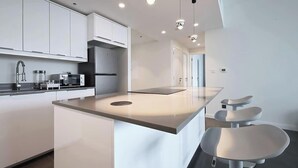 A modern kitchen with white cabinetry, a central island, and bar stools. - Golf Course Views Apt W Pool & Fast Wifi (Dubai)