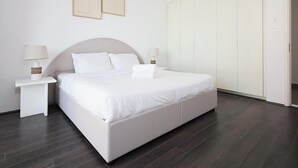 Une chambre moderne avec un grand lit, du linge de lit blanc, deux tables de chevet avec des lampes et une armoire.
