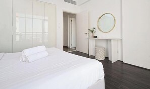A hotel room with a large bed, a mirror, a small fireplace, and a door leading to another room.