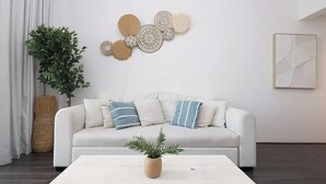 Un salon moderne avec un canapé blanc, des œuvres d’art décoratives au mur et une plante en pot posée sur une table basse.