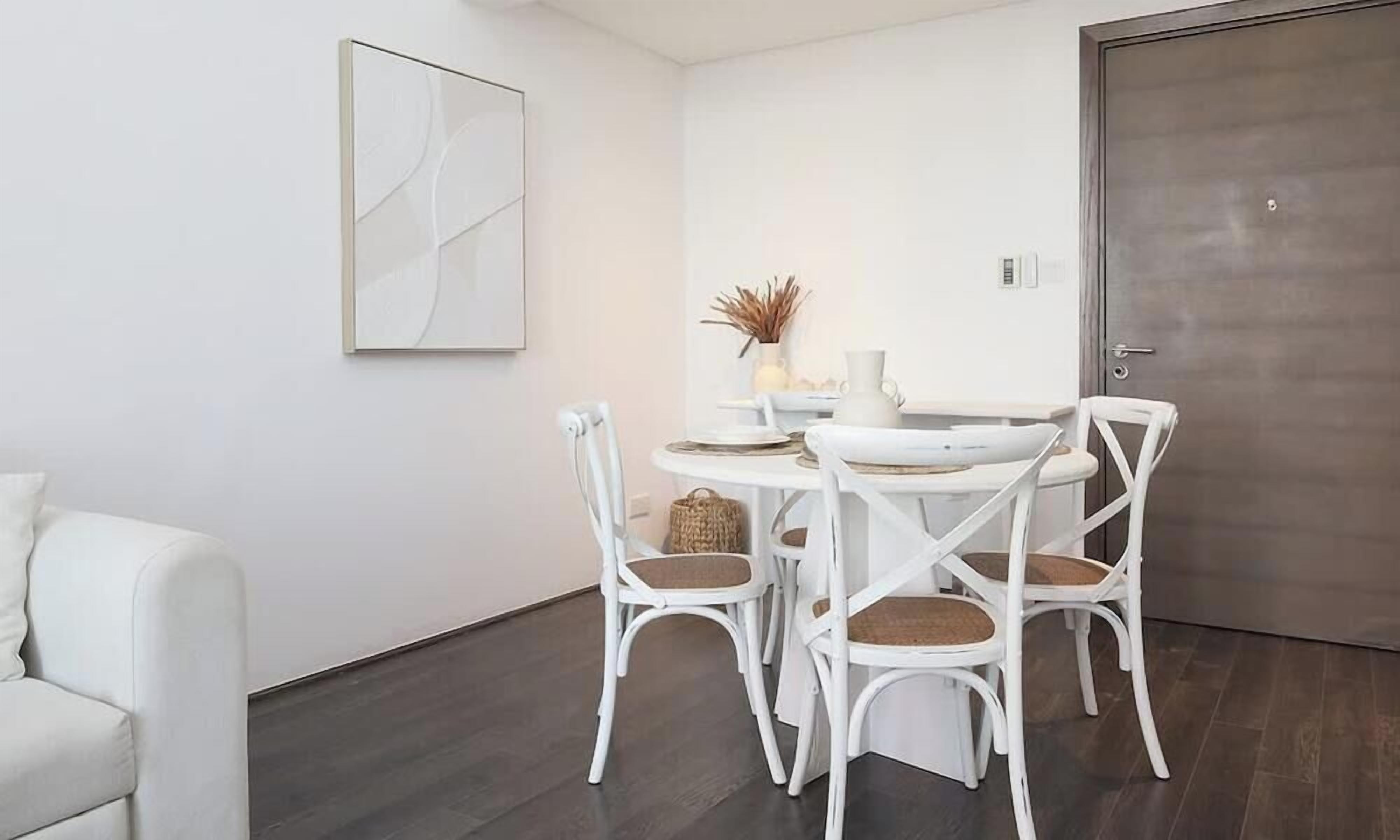 Comedor con una mesa redonda, sillas blancas y piso de madera oscura.