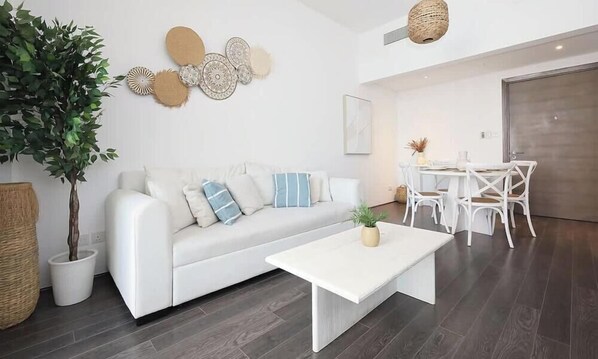 Ein modernes Wohnzimmer mit einem weißen Sofa, einem Couchtisch und einem Essbereich mit weißen Stühlen und einem Tisch.