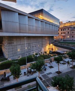 A modern building with a glass facade and a courtyard with trees and a paved walkway. - Acropolis View Deluxe Suite with Balcony (Athens)