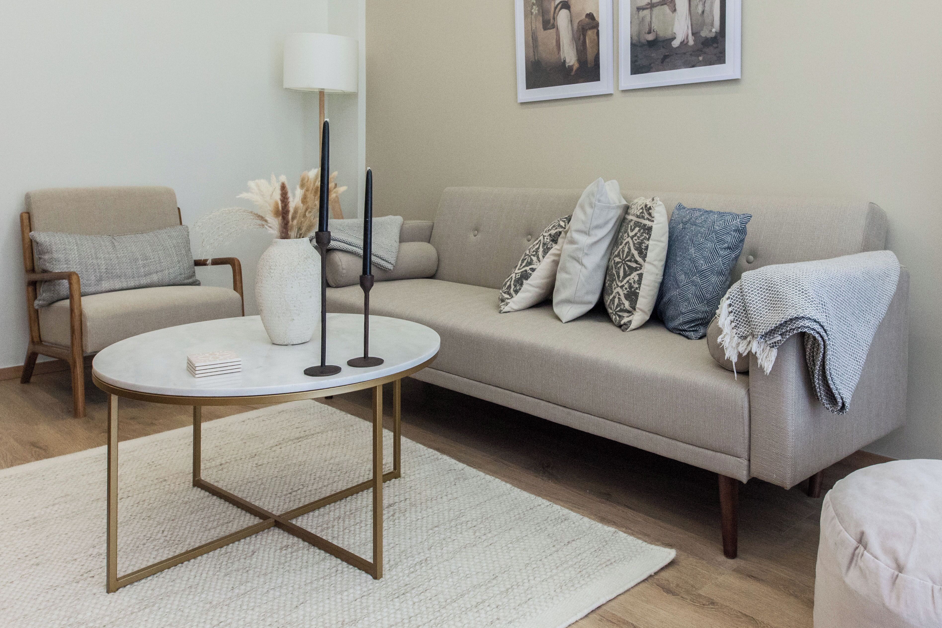 En stue med en beige sofa, et rundt sofabord, en hvid vase med pampas og to sorte lys.
