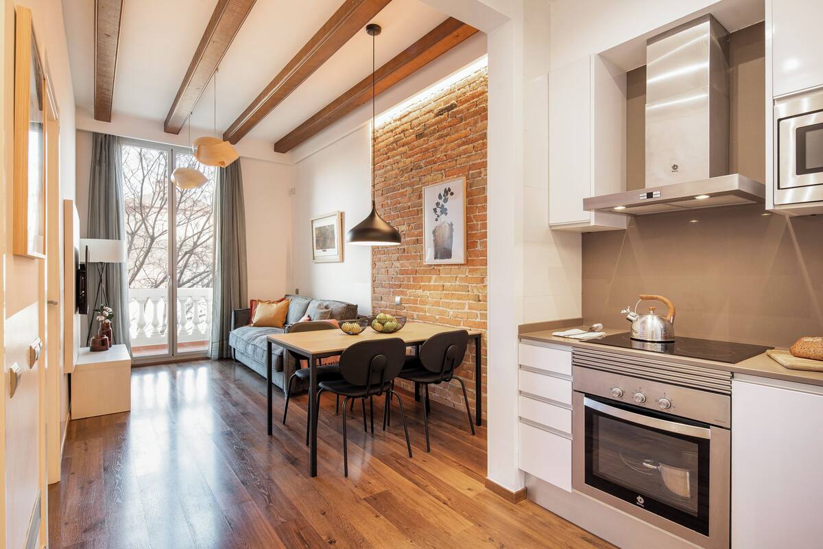 A modern kitchen with a brick wall, wooden beams, and a stainless steel oven.