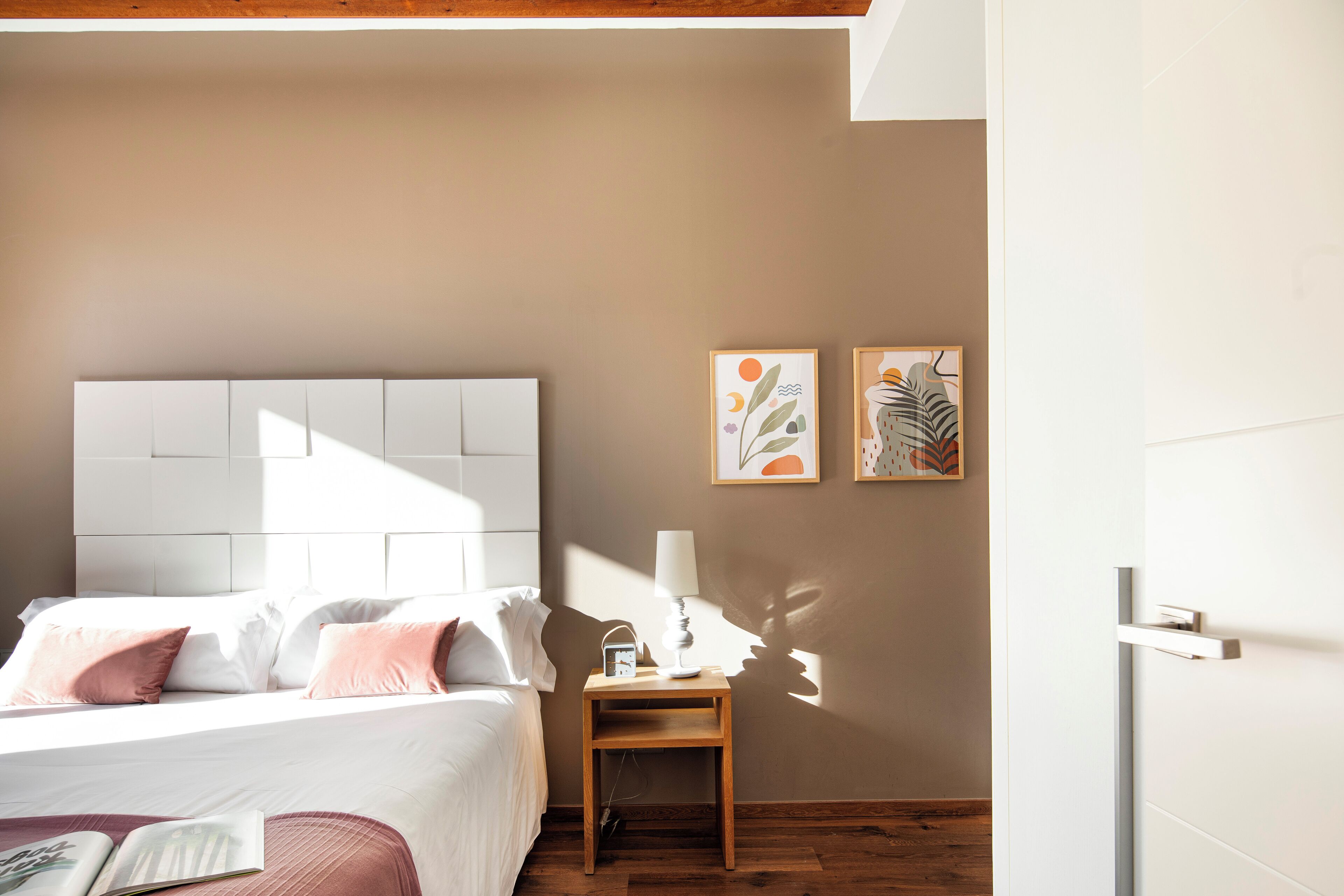 A bedroom with a bed, bedside table, lamp, and artwork on the wall.