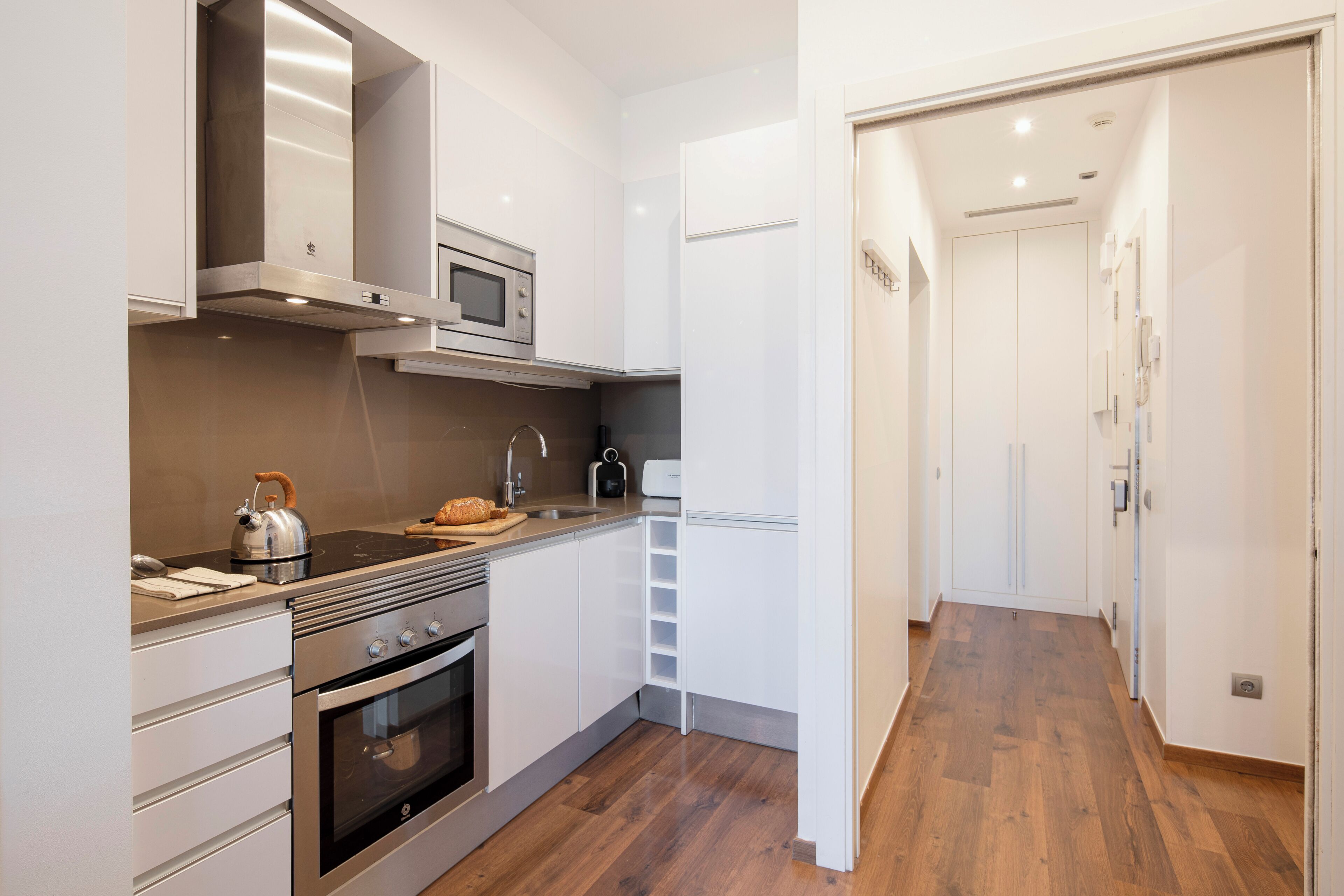 A modern kitchen with stainless steel appliances, a wooden floor, and white cabinetry.