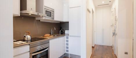 A modern kitchen with stainless steel appliances, a wooden floor, and white cabinetry.