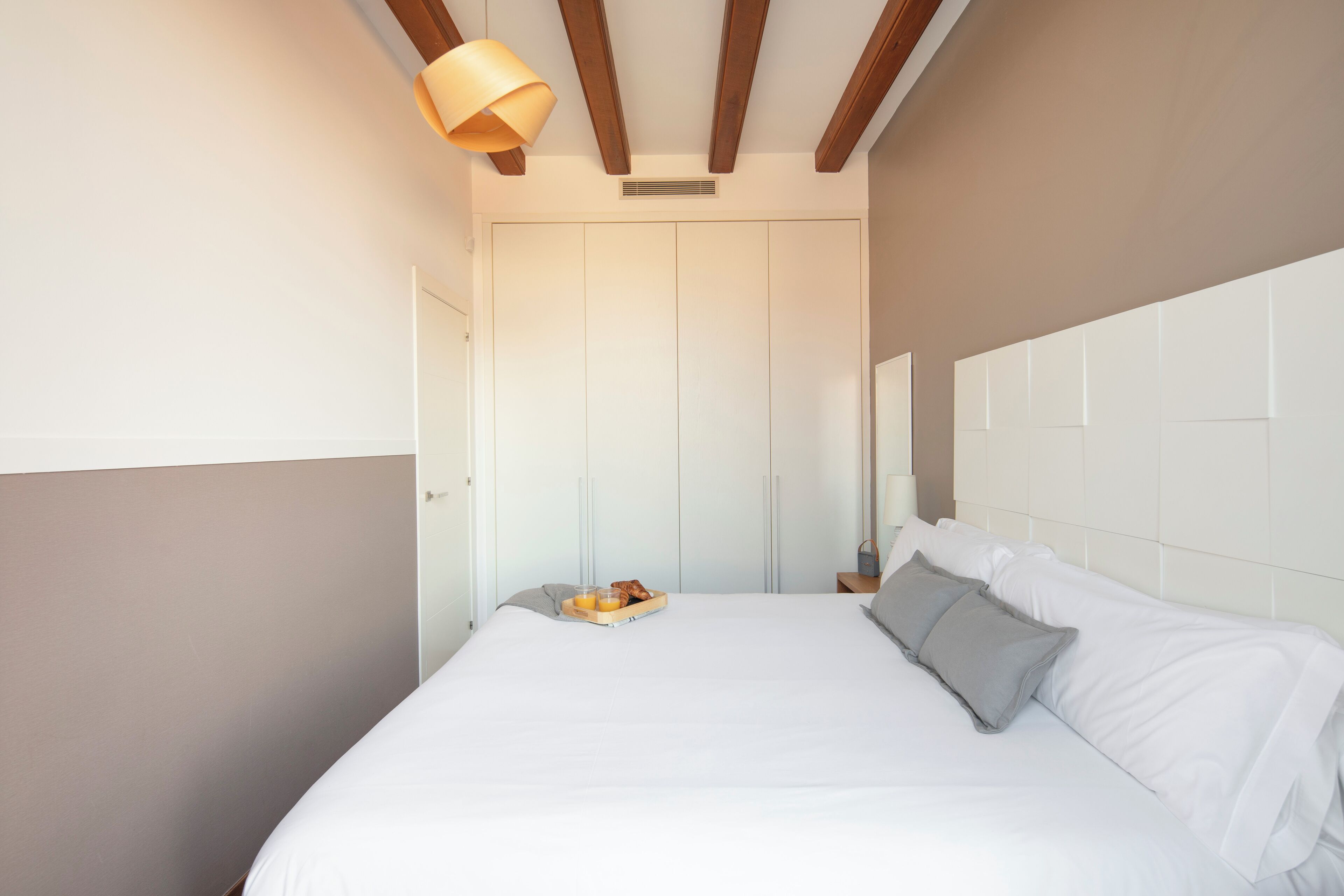 A neatly made bed with a tray of breakfast items, a bedside lamp, and a wooden ceiling beam.