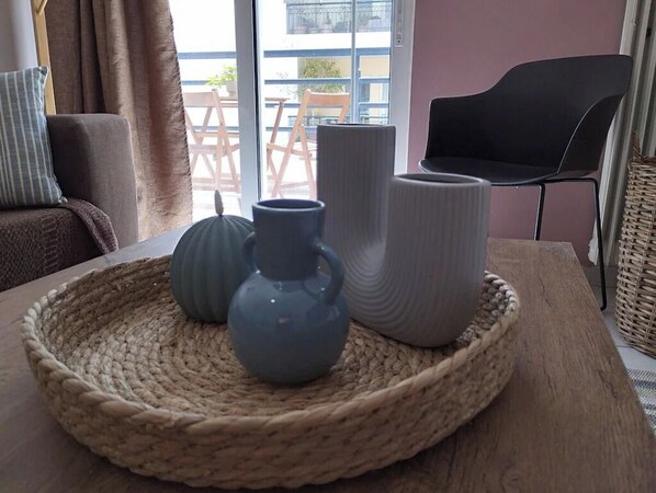 A round woven tray with three ceramic vases on a wooden table in a room with a view of the outside.