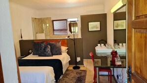 A bedroom with a bed, bedside table, lamp, and a small kitchenette area. - St Michelle Guest Lodge (Alberton)