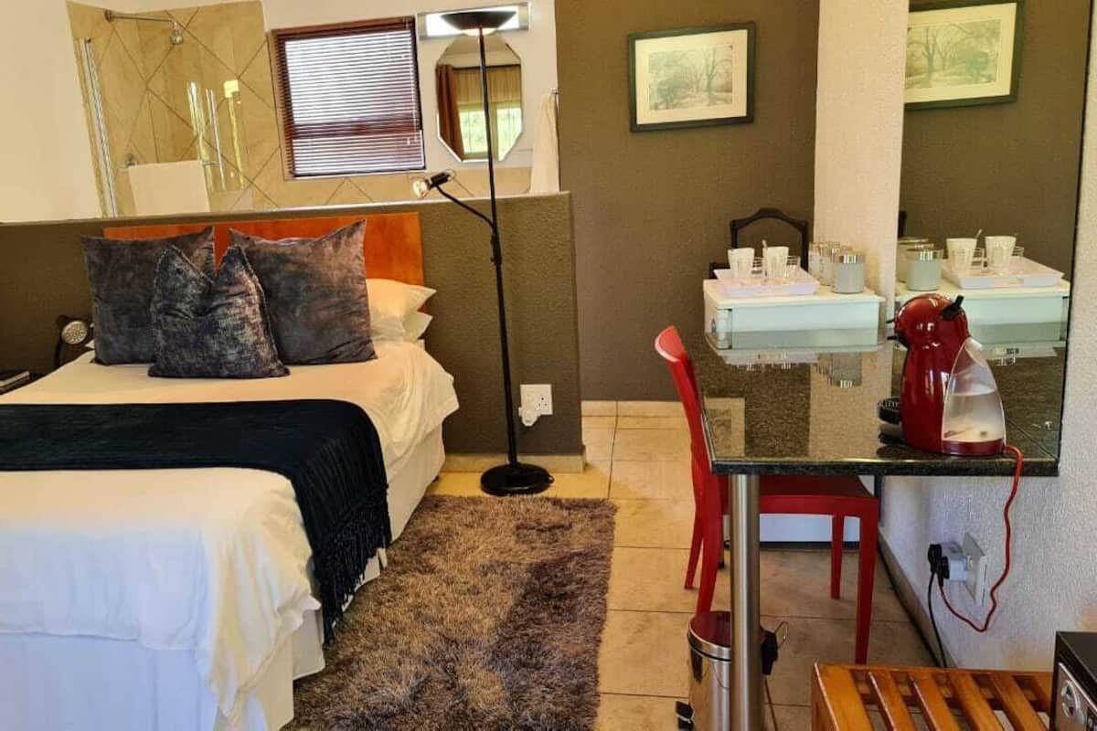 Une chambre comprenant un lit, une table de chevet, une lampe et un petit coin cuisine équipé d’une machine à café.