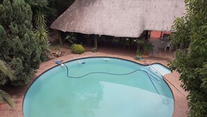 A circular pool with a thatched roof structure nearby. - St Michelle Guest Lodge (Alberton)