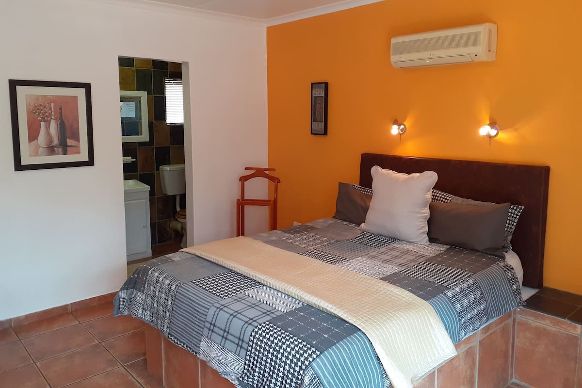 Une chambre à coucher comprenant un lit, une table de chevet, un climatiseur fixé au mur et un tableau encadré accroché au mur.
