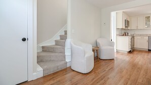 A modern apartment with a staircase, two armchairs, a small round table, and a kitchen area.
