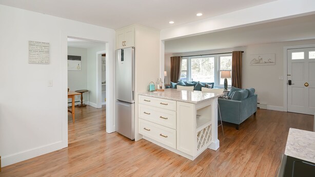 A modern kitchen with a built-in refrigerator, a dining area with a blue sofa, and a hallway leading to other rooms.