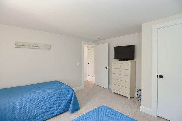 A bedroom with two beds, a dresser, a television, and a door leading to another room. - Just For The Halibut: Explore Folly Cove and Halibut Point State Park (Rockport)