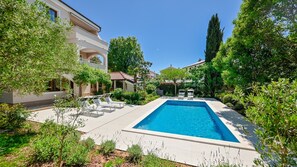 A swimming pool surrounded by lush greenery and a multi-story building with balconies. - Modern Apartment Lara (Malinska - Rijeka Region)