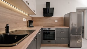 Una cocina moderna con un refrigerador de acero inoxidable, horno empotrado, cafetera y un lavabo.