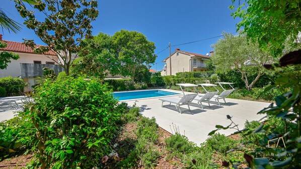 A swimming pool with lounge chairs, surrounded by lush greenery and residential buildings. - Modern Apartment Lara (Malinska - Rijeka Region)