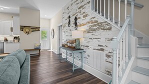 Una sala de estar moderna con piso de madera, una escalera con barandilla blanca y una pared rústica con pintura desgastada.