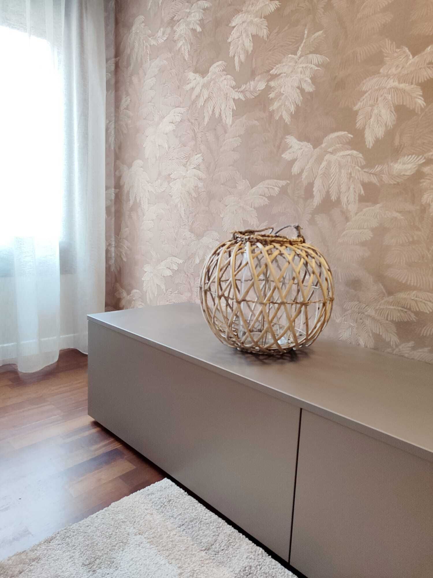 A room with a grey console table, a woven basket on top, a white rug, and a window with sheer curtains.