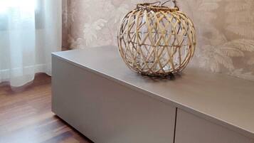 A room with a grey console table, a woven basket on top, a white rug, and a window with sheer curtains.